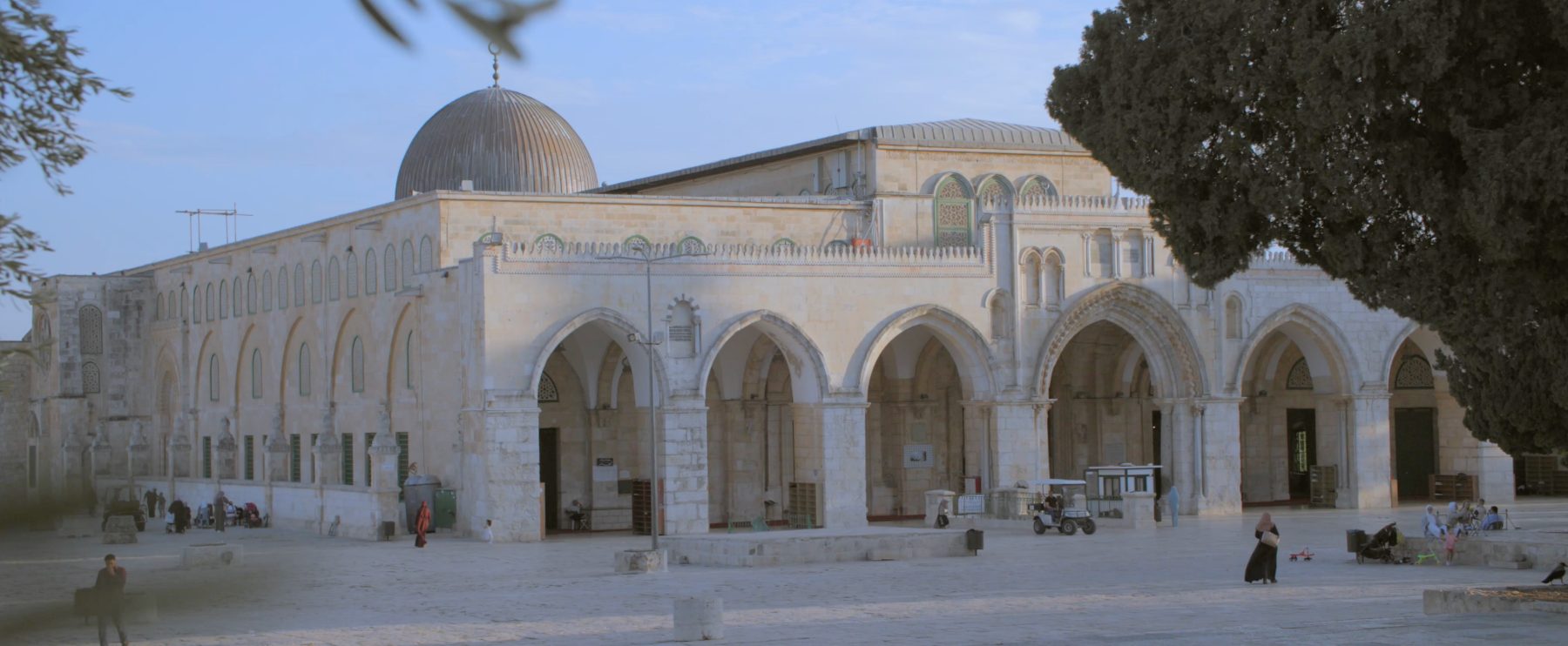 The arched stone facade of the Qibli Mosque, worshippers resting in its shade